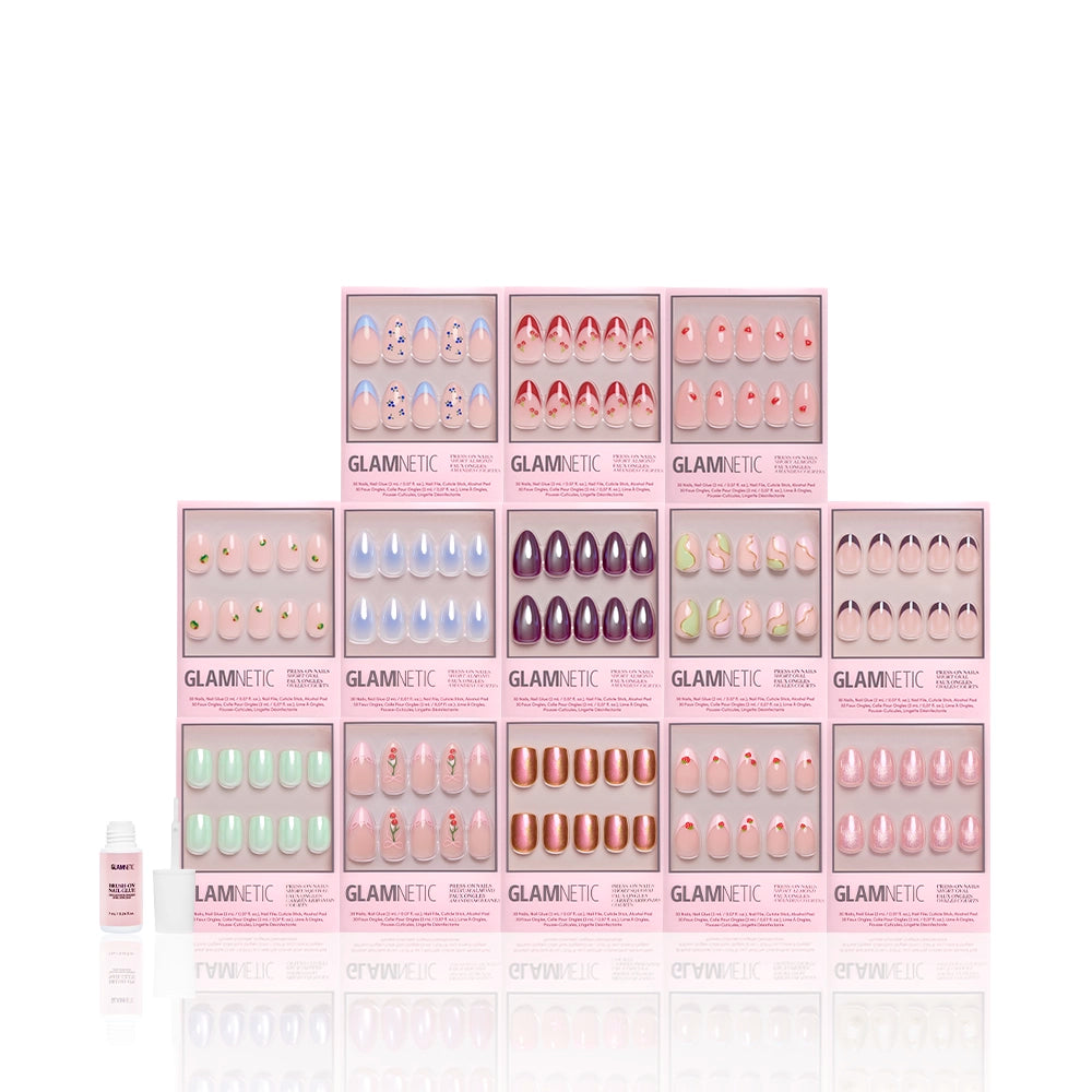 Twelve glamnetic The Juicy Drop Collection press-on nail sets in pastel and metallic glossy shades are arranged in three rows on a clean, reflective white background, with a small nail glue bottle displayed in front on the left. - Product image