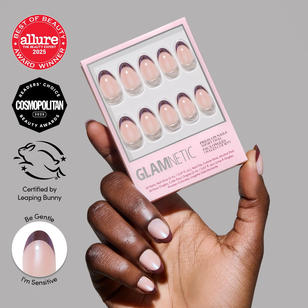 A hand with medium brown skin holds a box of glamnetic Cherry Mood press-on nails in a subtle mauve French tip design. Beauty award logos and a close-up of the short oval nails style appear on the left side of the image.