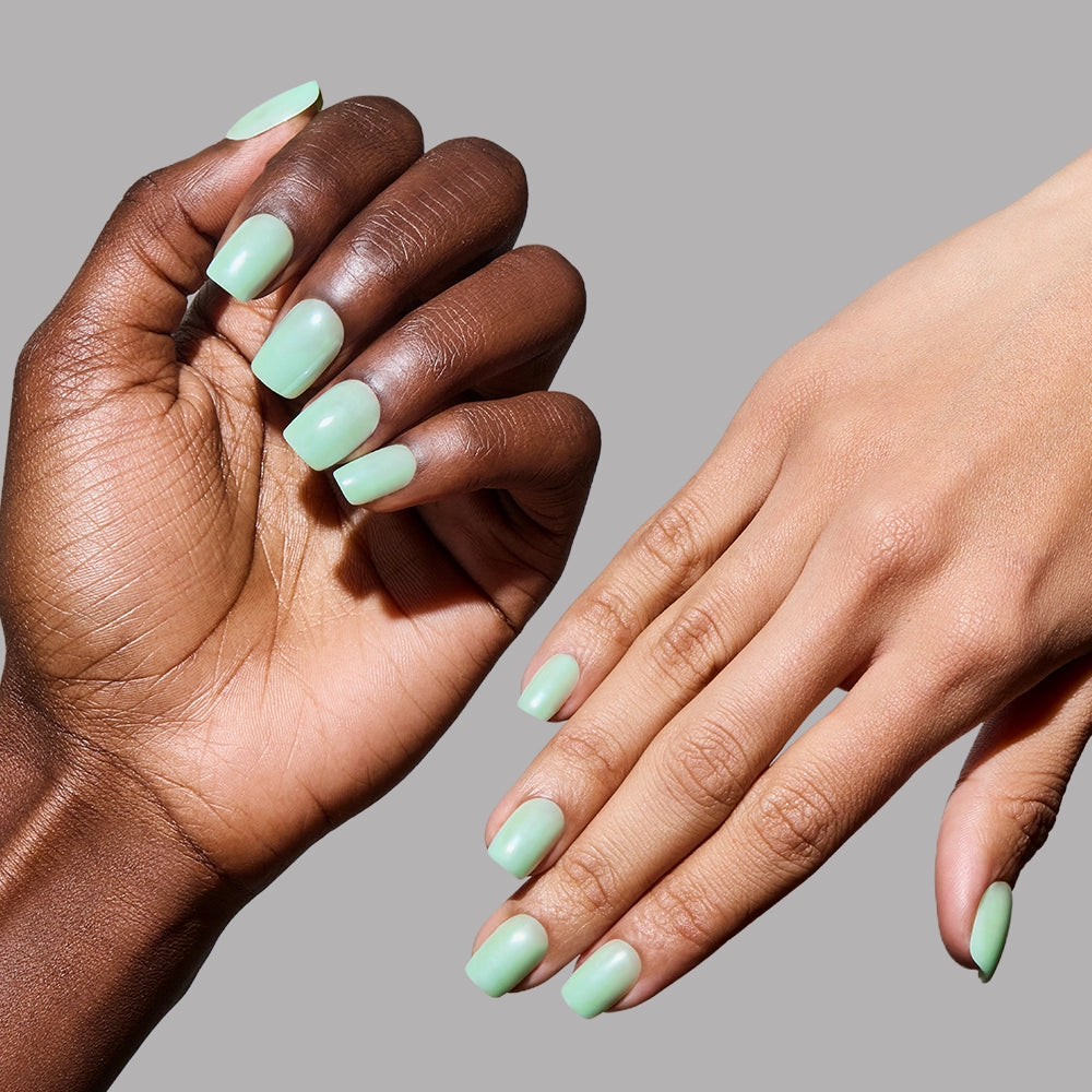 Two hands—one with a dark and one with a light skin tone—display mint green nails in "Honeydewy" by glamnetic, a vibrant vegan, cruelty-free polish, set against a plain gray background. - Product image