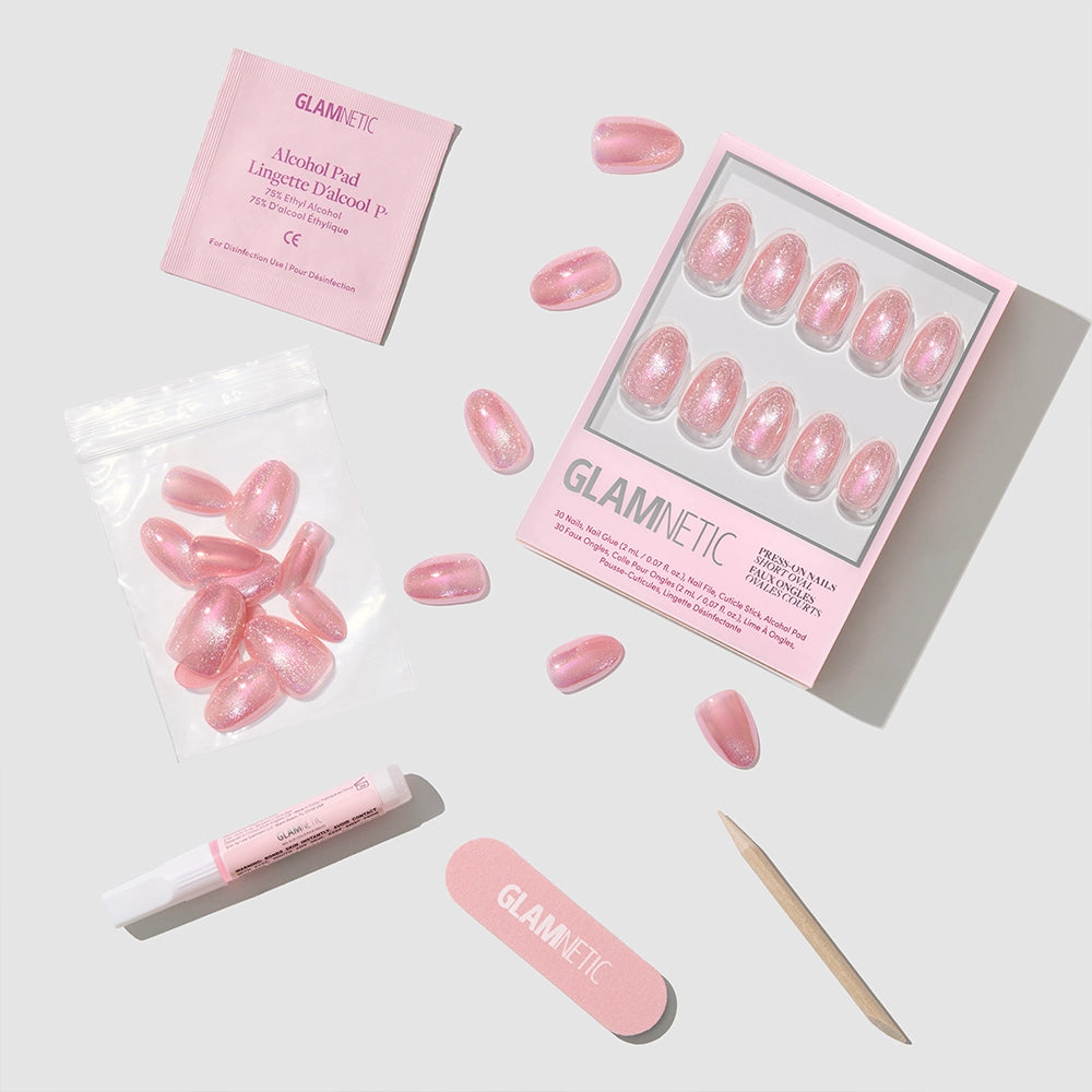 A flat lay of the glamnetic Guava Drop press-on nails kit featuring short oval, glittery glazed nails, glue, nail file, cuticle stick, alcohol pad, and extra nails in a plastic bag—all displayed on a light gray background. - Product image
