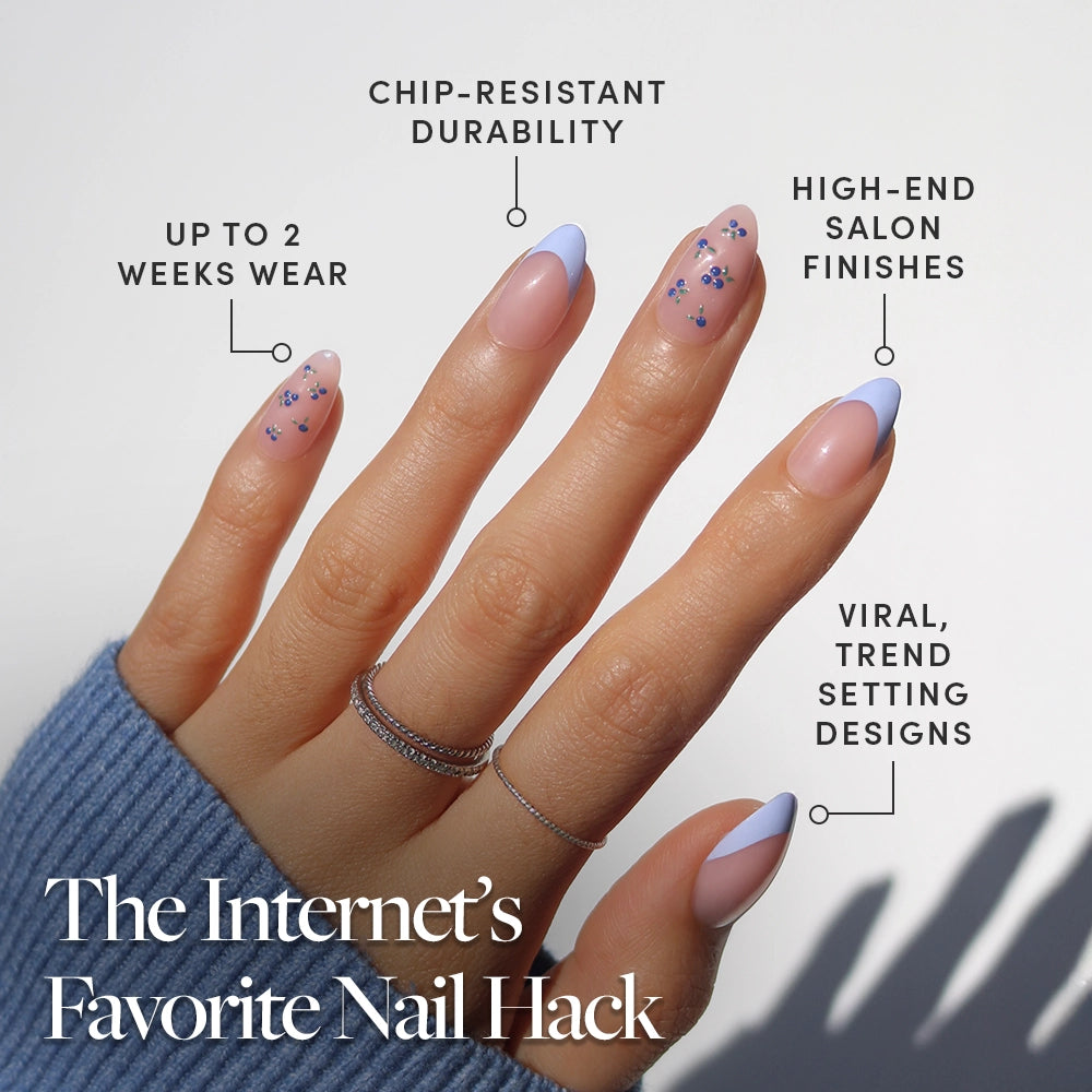 A hand with almond nails in Bluebelle by glamnetic showcases light blue French tips and floral art, boasting up to 2 weeks' wear, chip-resistant durability, high-end salon finish, and viral, trend-setting design. - Product image