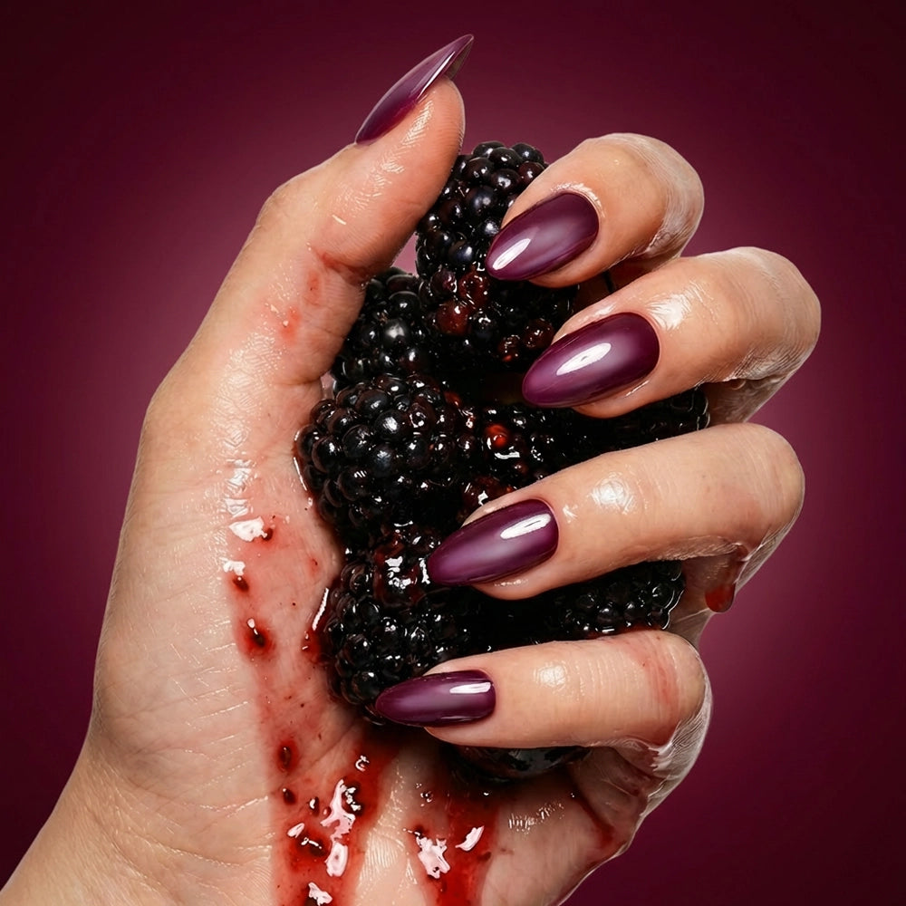 A hand with glossy purple, almond-shaped Jam Drizzle nails by glamnetic squeezes ripe blackberries, their juice dripping down the fingers against a deep purple background. - Product image