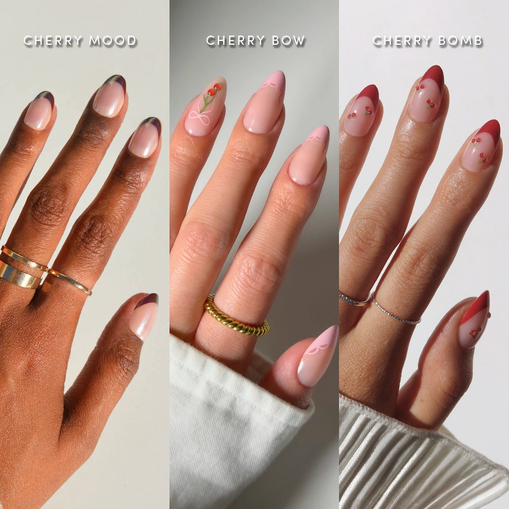 Three hands display glamnetic’s Cherry On Top nail set: it features French tips with thin dark outlines, pink nails adorned with tiny cherry and bow designs, and almond-shaped red tips decorated with small cherry patterns. - Product image