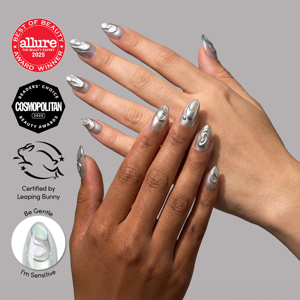 Two hands display long, almond-shaped nails with a shiny silver and white abstract swirl design using glamnetic’s Unicorn Blood. Award badges and cruelty-free certification logos appear on the left side of the image.