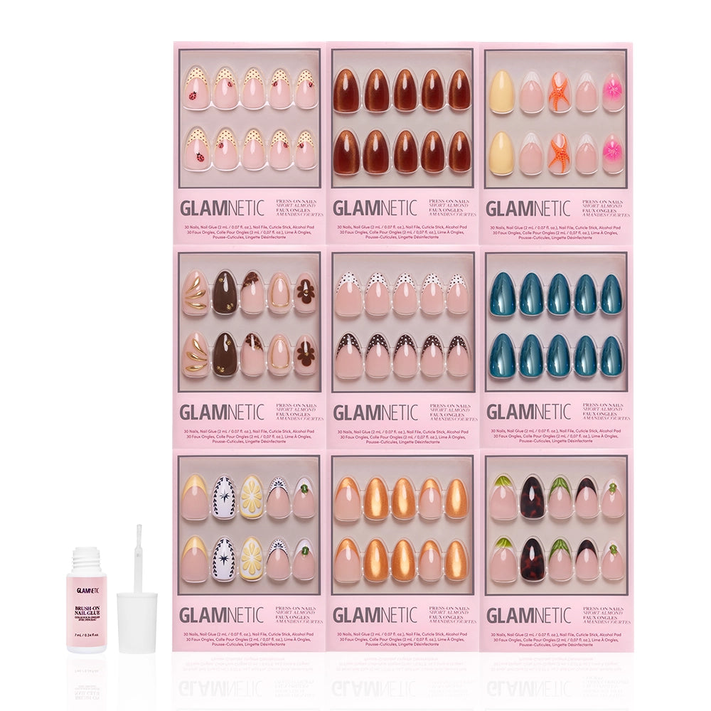 Nine Glamnetic Almond Amore press-on nail sets featuring florals, patterns, and solid colors are arranged in a grid. In front are a pink bottle of nail glue and an applicator, with chic almond shapes and French tip designs from the brand glamnetic. - Product image