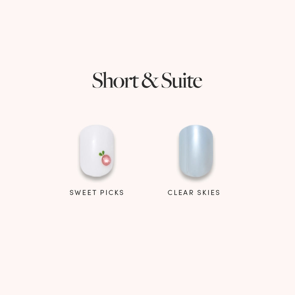 Two salon-quality glamnetic press-on nails from the Short & Suite set are shown: a white nail with a pink cherry design called Sweet Picks, and a shiny pale blue nail called Clear Skies.