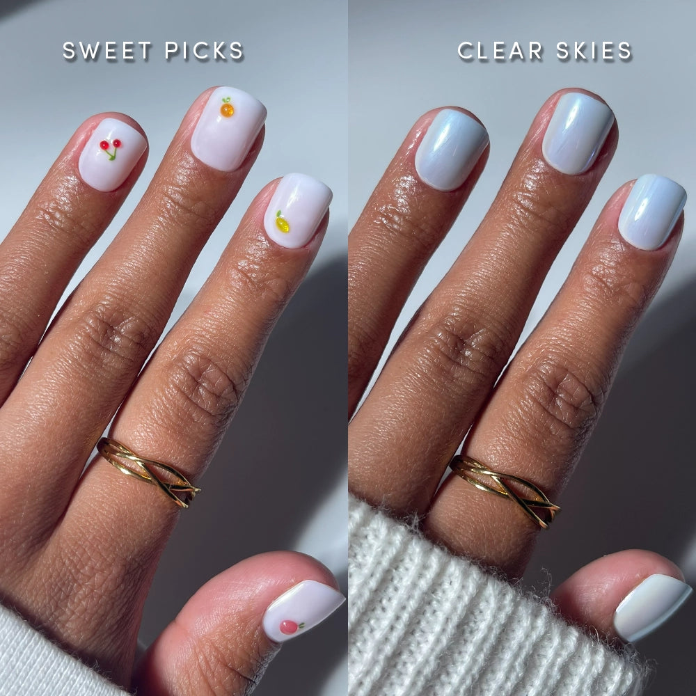 A hand with a gold ring shows two glamnetic Short & Suite salon nails: left side features white press-ons with colorful fruit art, labeled SWEET PICKS; right side has glossy pale blue nails, labeled CLEAR SKIES.