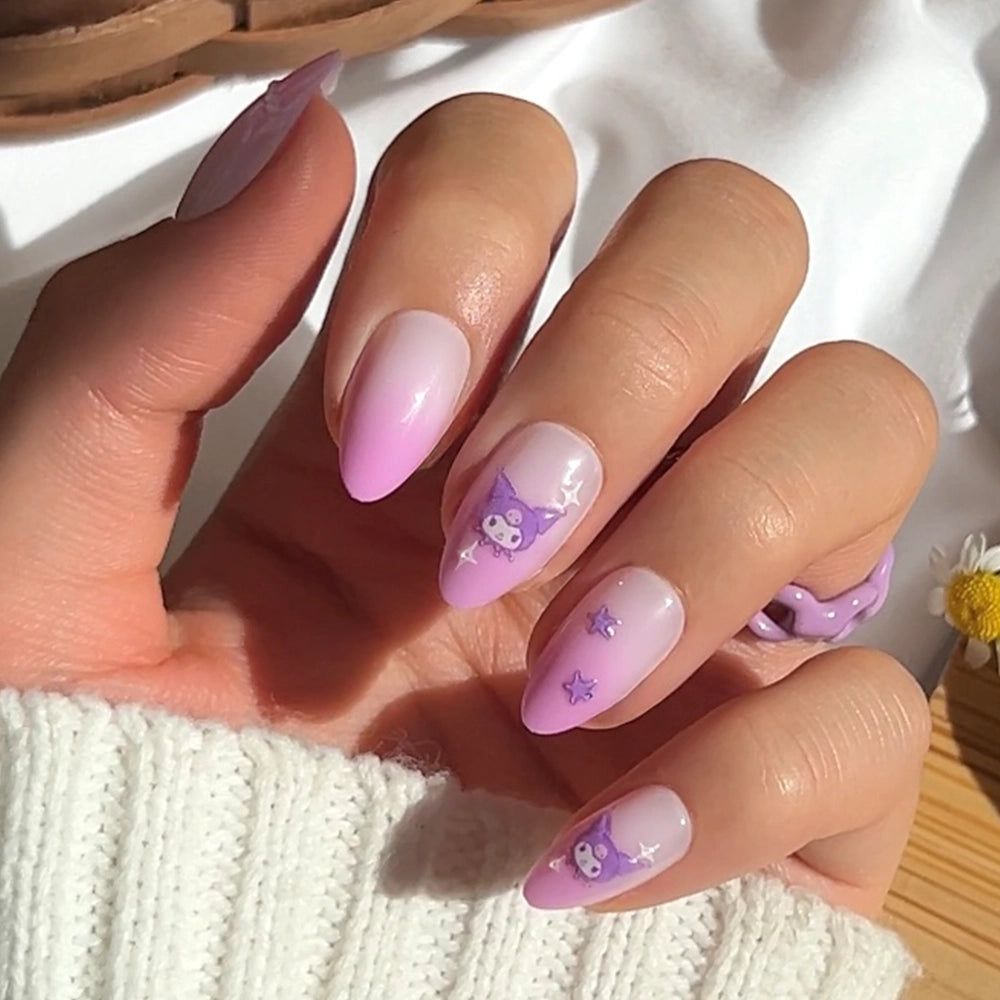 A hand with short almond nails painted in a pink and purple ombre, featuring glamnetic's Kuromi™ cartoon characters, star designs, playful 3D accents, a white sweater, and a lilac ring for an elevated look.