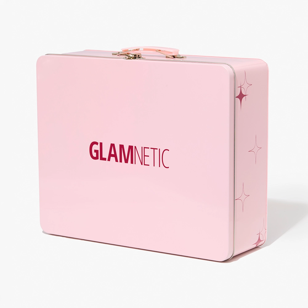 The Quick Press Mani PR Box by glamnetic is a light pink rectangular metal suitcase with a gold handle and clasp, bold red and pink "GLAMNETIC" on the front, star designs on the side—ideal for storing your quick press mani or no-glue press-on nails.