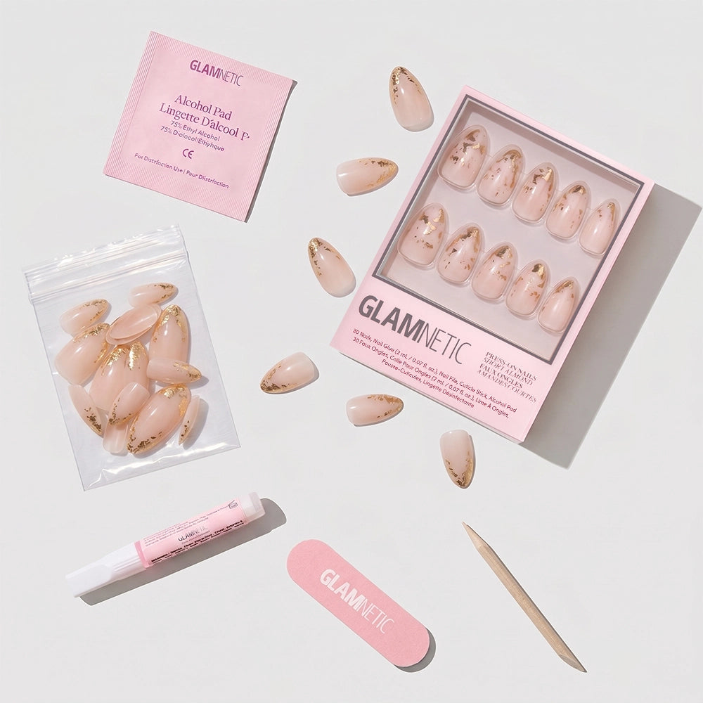 The glamnetic 24K set features short almond pink and gold foil press-on nails, nail glue, a wooden cuticle stick, a pink nail file, an alcohol pad, and extra nails—all arranged on a white surface. - Product image