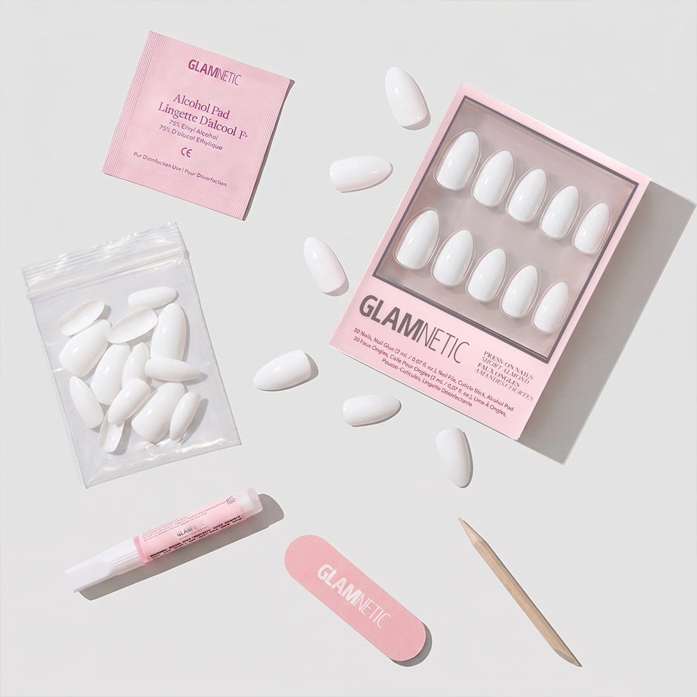 A flat lay of the glamnetic Angel press-on nails kit, featuring short almond white nails, glue, a wooden cuticle stick, nail file, alcohol pad, and extra nails—all neatly arranged on a light surface. - Product image