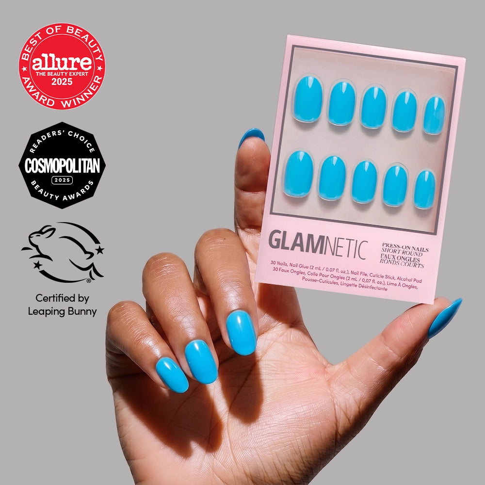 A hand with bright blue, glossy short round glamnetic Azure Blue press-on nails holds the box. Allure and Cosmopolitan beauty awards and a Leaping Bunny cruelty-free badge emphasize their long-lasting wear.