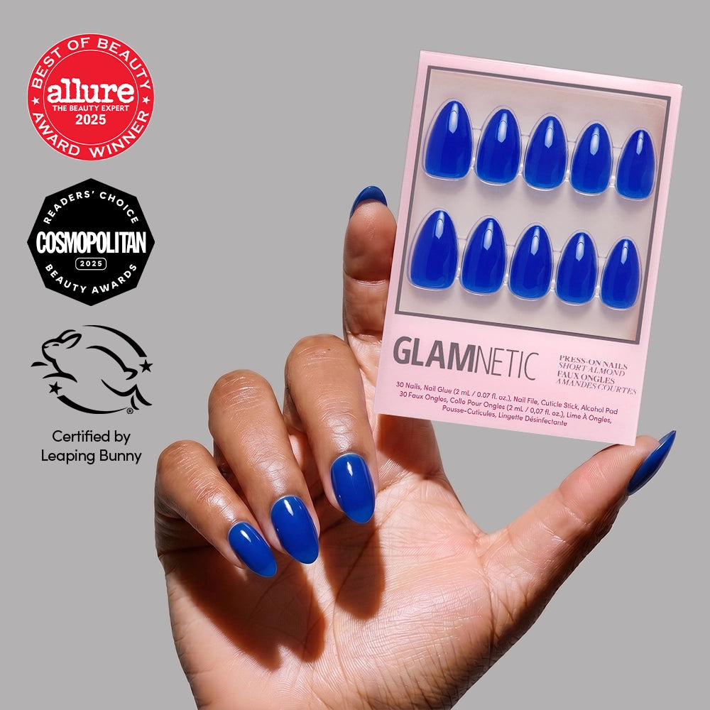 A hand with glossy, short almond Cobalt Blue press-on nails by glamnetic holds a matching package. Allure, Cosmopolitan, and Leaping Bunny award logos on the left spotlight these chic summer nail designs.
