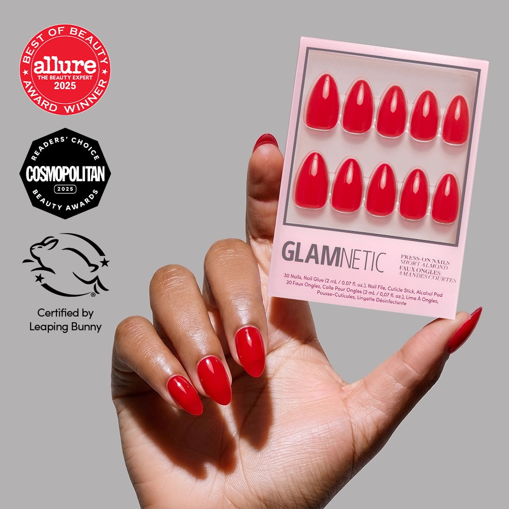 A hand with glossy Fiery Red glamnetic press-on nails holds the nail set package, showcasing summer-ready shine. Beauty award logos from Allure (2025), Cosmopolitan (2023), and a Leaping Bunny cruelty-free mark appear on the left.