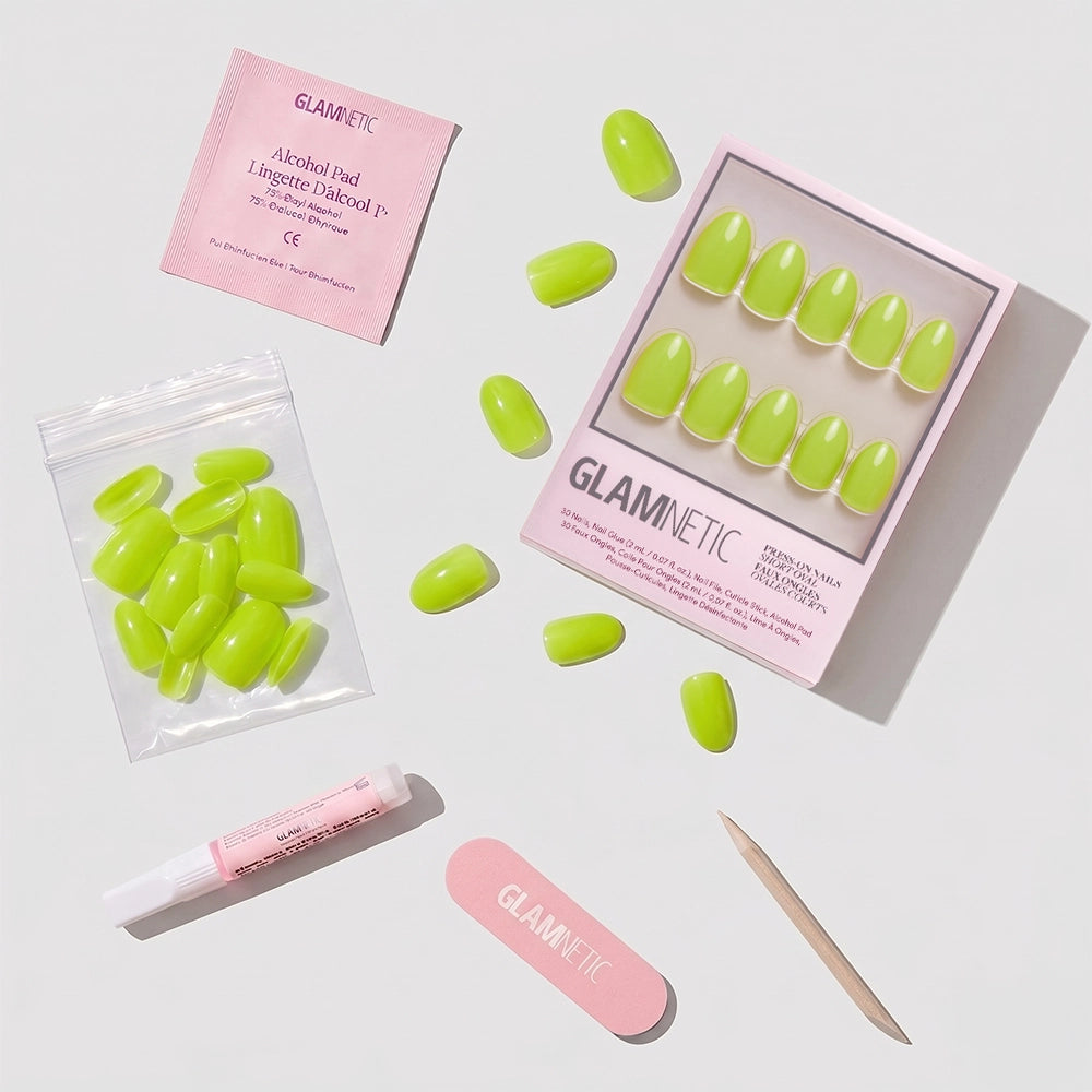 The glamnetic Lime Green set includes bright short oval press-on nails, glue, a pink nail file, cuticle stick, alcohol pad, and extra vegan cruelty-free nails, all neatly arranged with branded packaging. - Product image