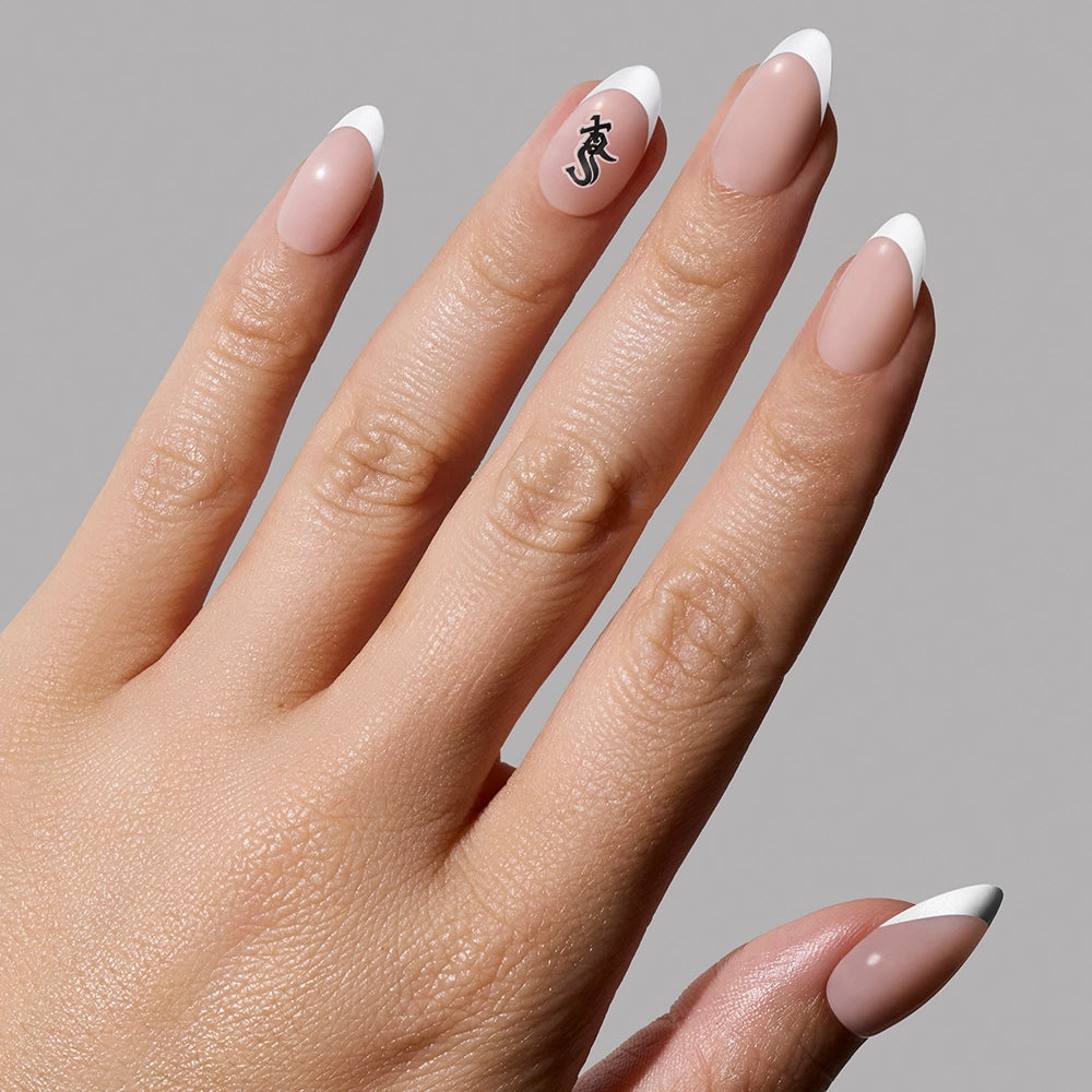 A hand displays the glamnetic Chicago White Sox Press-On Nail Set featuring long, almond-shaped, French tips with a team-inspired black design on the ring finger, all set against a plain gray background.