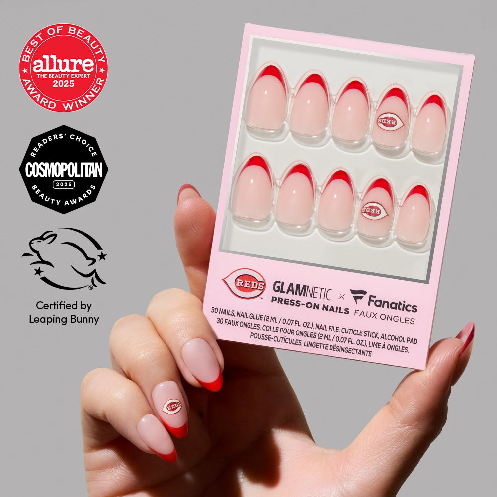 A hand holds a box of glamnetic Cincinnati Reds Press-On Nail Set. Beauty award badges and a cruelty-free Leaping Bunny certification are displayed on the left side of the image.