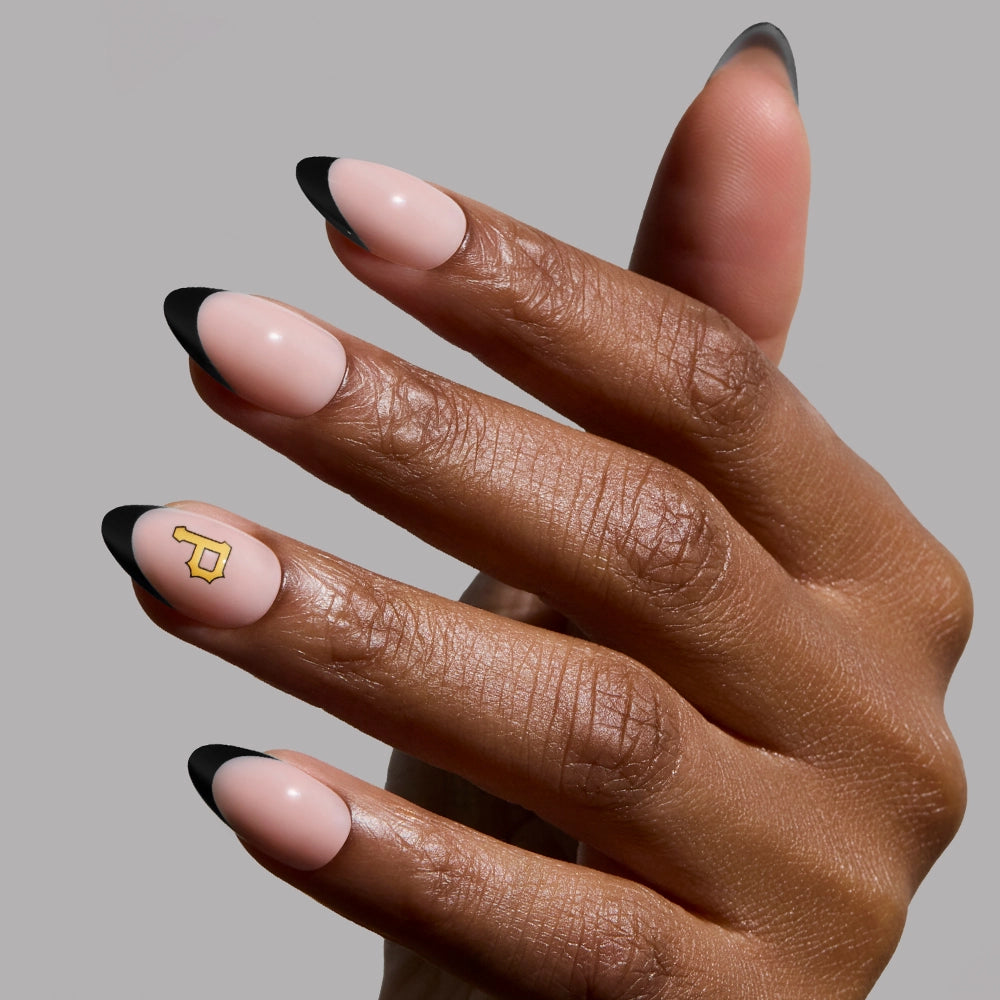 A hand with a Pittsburgh Pirates Press-On Nail Set by glamnetic features nude nails with black tips, while the ring finger showcases a minimalist gold key design, creating a chic and glossy manicure.