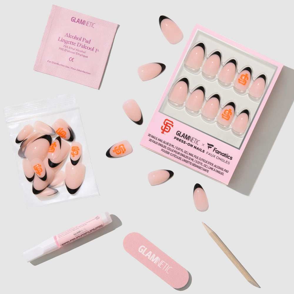 The glamnetic San Francisco Giants Press-On Nail Set, including pink and black press-on nails, nail glue, an alcohol pad, a nail file, a cuticle stick, and extra nails, is neatly arranged on a light gray background. - Product image