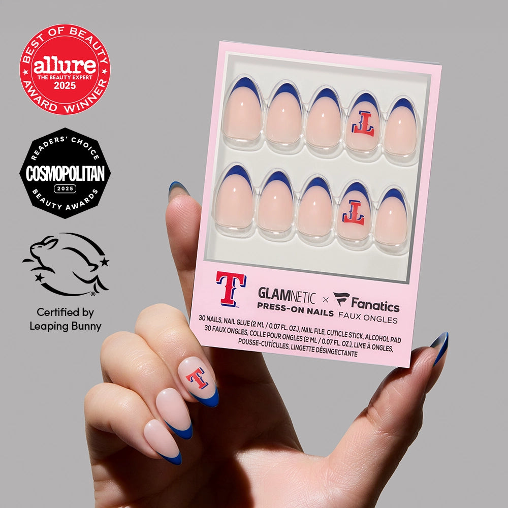A hand shows off short almond Texas Rangers Press-On Nails by glamnetic, holding the officially licensed set box. Allure, Cosmopolitan, and Leaping Bunny award badges appear on a neutral background.