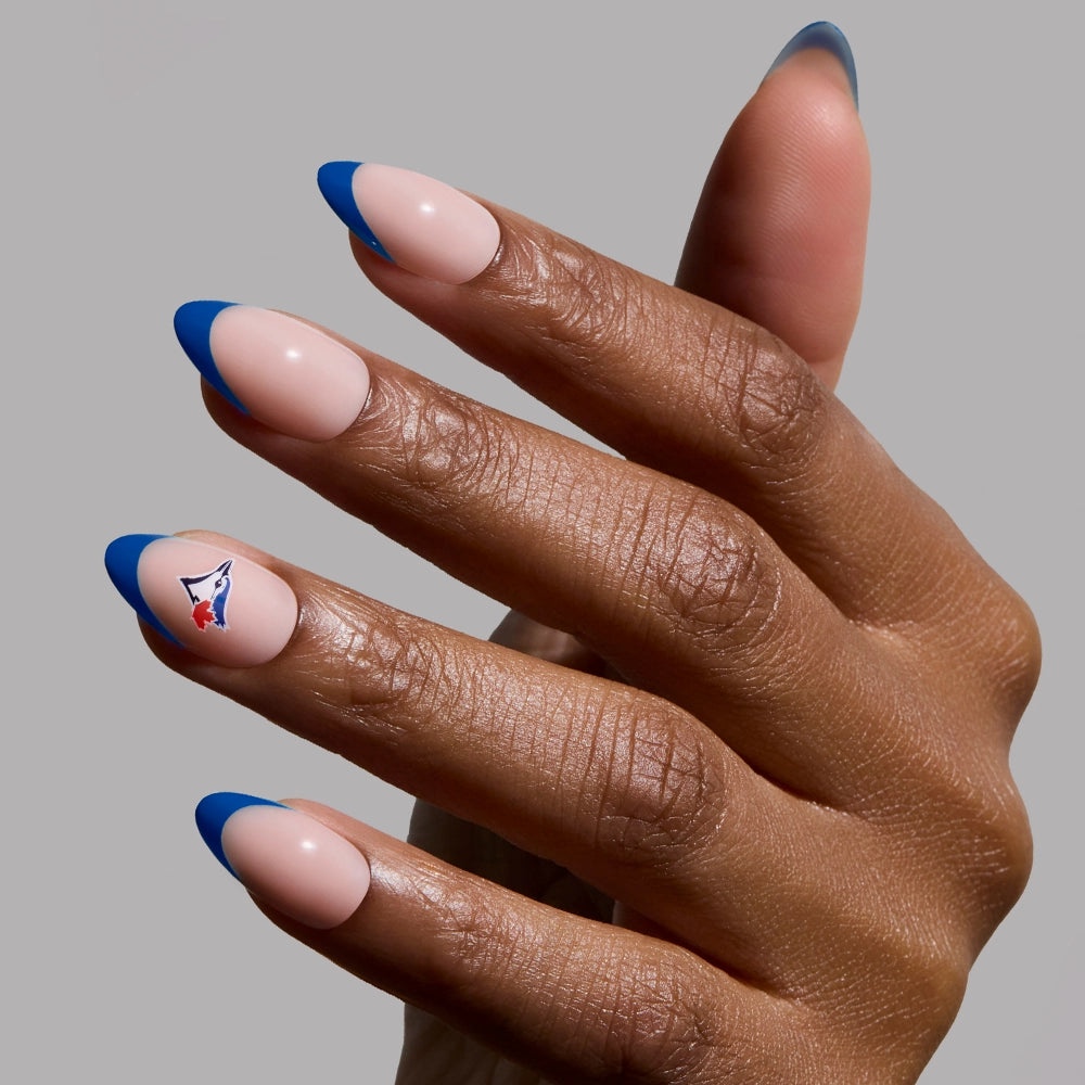 A hand with glamnetic's Toronto Blue Jays Press-On Nail Set—short almond nails with a nude base, bold blue French tips, and an abstract blue, red, and white design on the ring finger—perfect for Blue Jays fans.