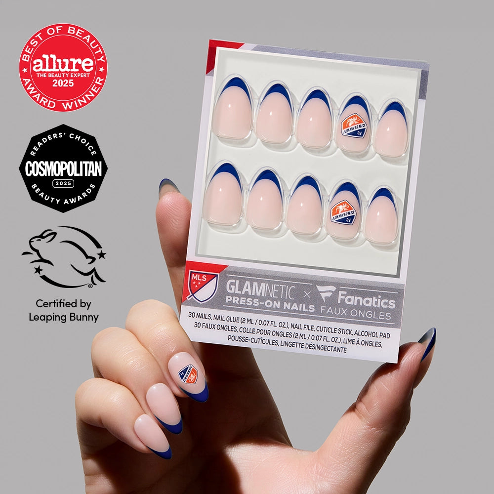 A hand holds the FC Cincinnati Press-On Nail Set by glamnetic, featuring blue French tips and team logos. Allure 2025, Cosmopolitan 2023, and Leaping Bunny vegan press-on nails certification badges are shown on the left.