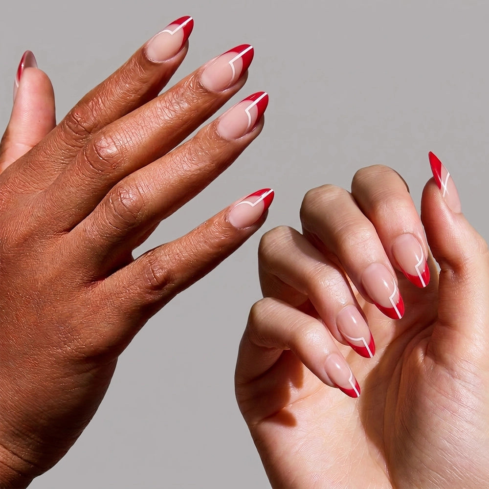 Two hands display glamnetic's Red Martini nails—short almond shape with a nude base, bold holiday red tips, and a thin white diagonal stripe near the edge—against a plain gray background. - Product image