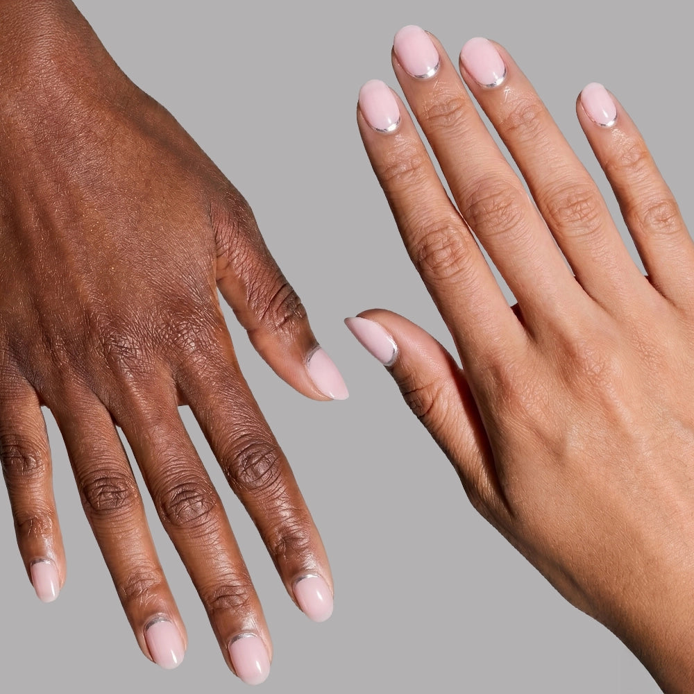 Two hands—one lighter, one darker skin tone—with short round nails in light pink and a minimalist silver half-moon design, showcase glamnetic's "Silver Belle" press-ons against a gray background. - Product image