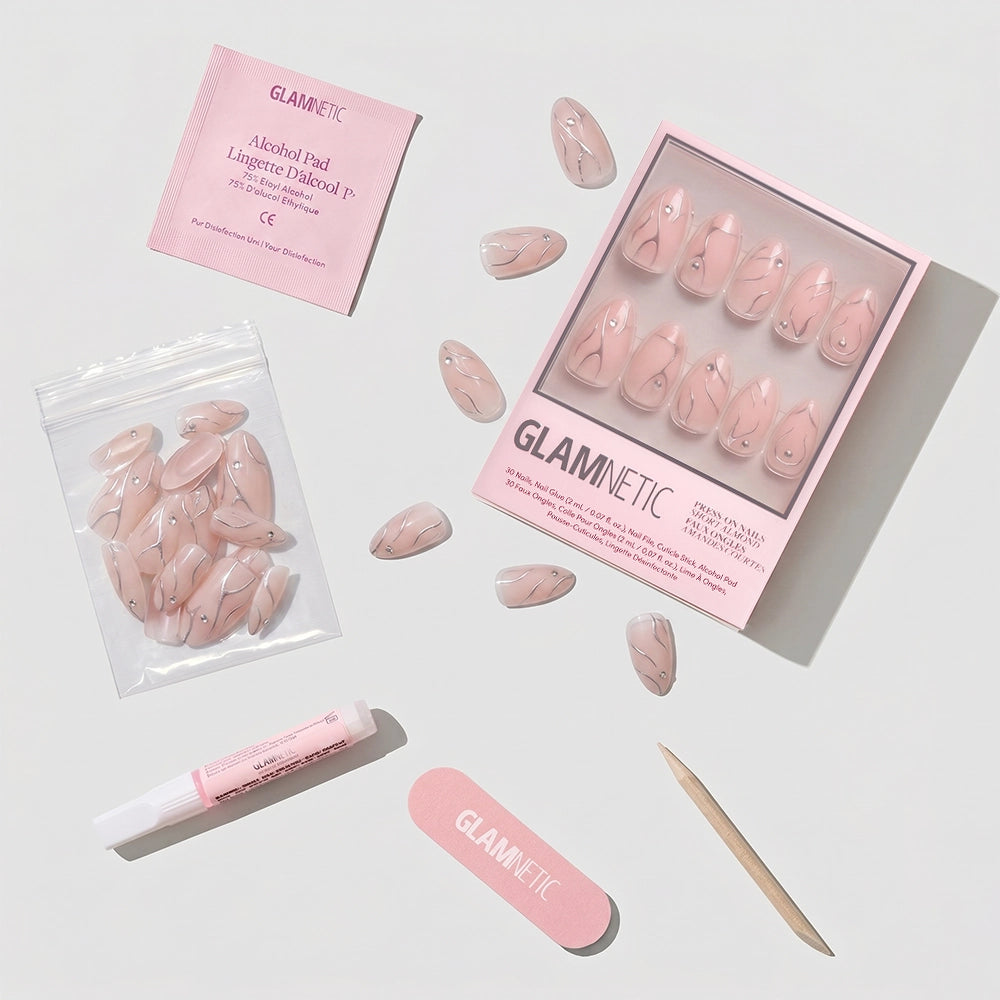 The Astro set by glamnetic features short almond press-on nails in a pink marble design. Each set includes an alcohol pad, nail glue, nail file, cuticle stick, and extra nails, all displayed on a white background. - Product image