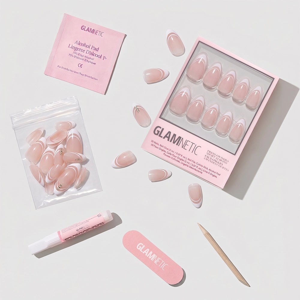 The Glamnetic Paris press-on nail kit is shown, with short almond nude nails, glue, a mini file, alcohol pad, cuticle stick, and extra nails—all neatly arranged on a white background. - Product image