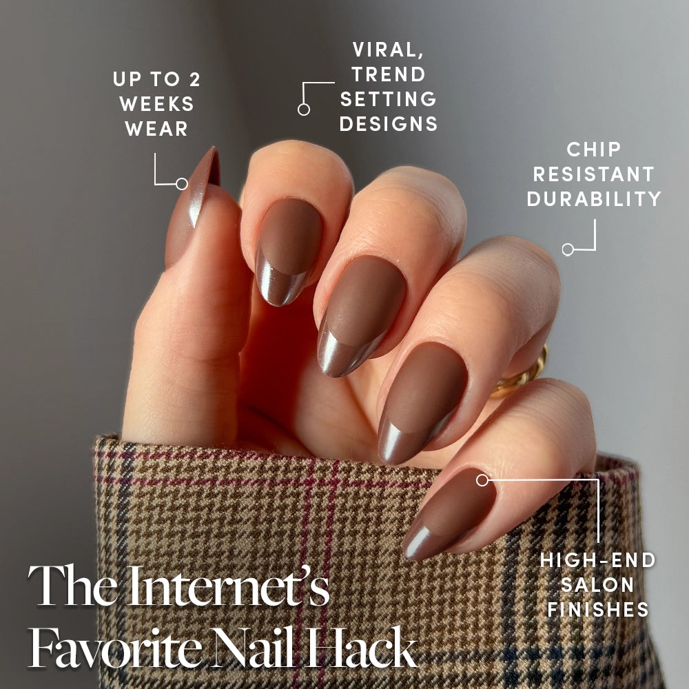 A hand with glamnetic Terra matte almond press-on nails in brown and metallic silver tips. These vegan nails last up to 2 weeks, feature viral designs, chip resistance, and luxe finishes. Shown against plaid fabric. - Product image