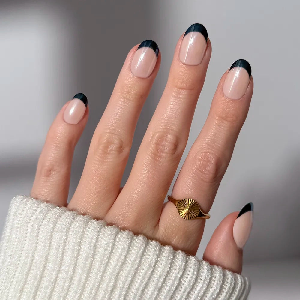 A hand with glossy, almond-shaped tips in Onyx Glaze by glamnetic rests against a white ribbed sweater, showing off black-tipped French nails and a gold ring. - Product image