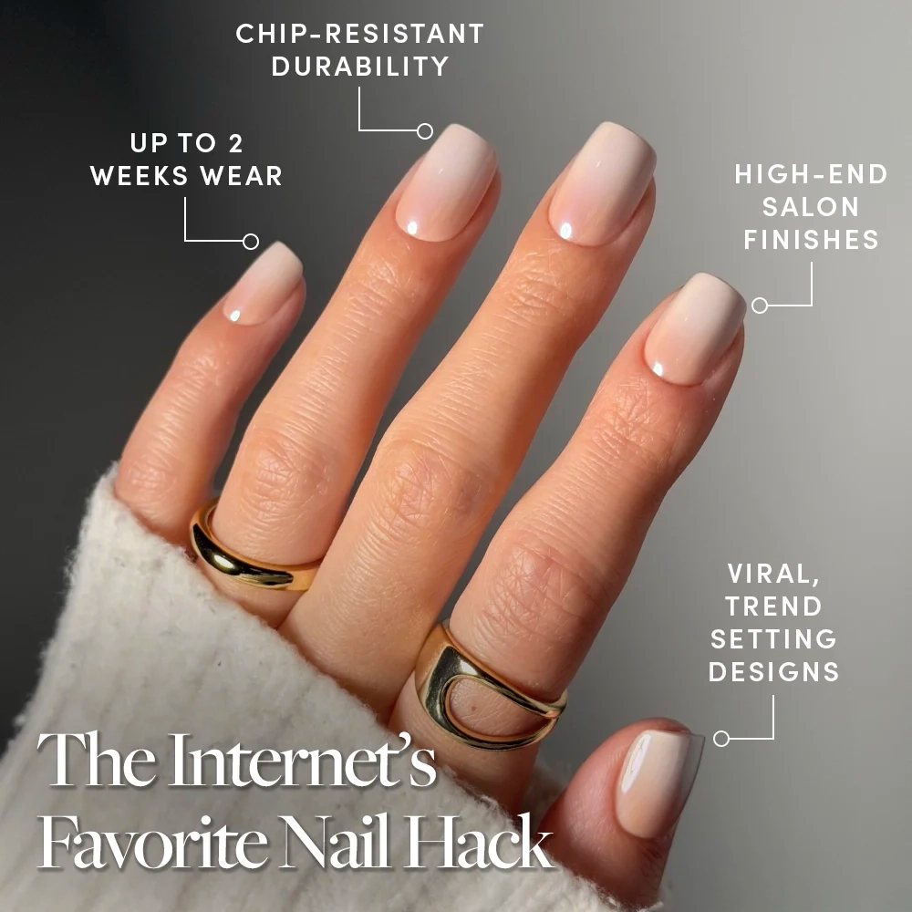 A hand wears glamnetic's Sugar Veil glossy nude ombré press-on nails, styled with gold rings and a white sleeve. Features include chip-resistant durability, trendy viral design, and up to 2 weeks of wear. - Product image