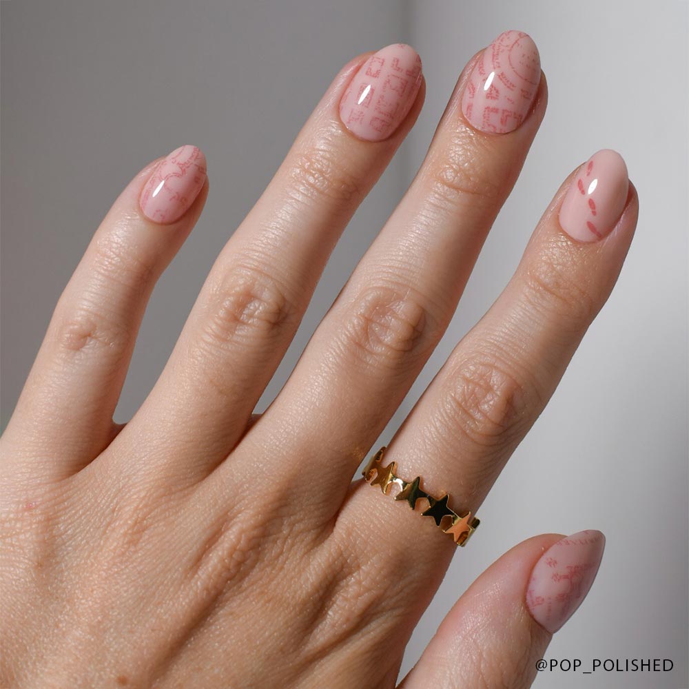 A hand with light pink Marauders Map™ nails by glamnetic, featuring a subtle geometric line design. The person wears a gold ring with small black star shapes on their middle finger. - Product image
