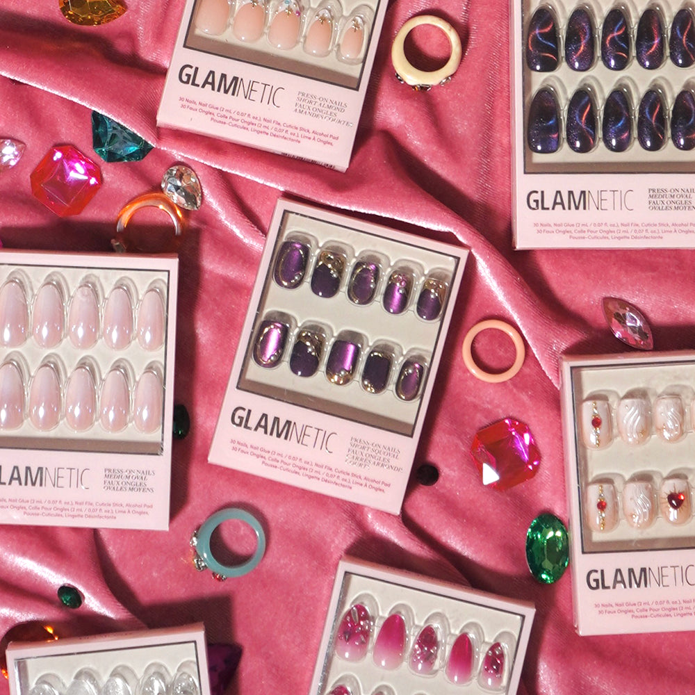 Glamnetic’s Amethyst Press-On Nails, featuring a luxurious velvet finish, along with an array of chic short squoval press-on nail sets in different colors and styles, are artfully displayed on soft pink satin fabric, accented by decorative rings and vibrant gem-like ornaments. - Product image