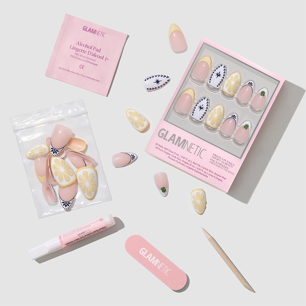 The glamnetic Aperitivo Hour set features short almond press-on nails in pastel designs, a pink nail file, wooden cuticle stick, nail glue, alcohol pad, and extra nails displayed on a light gray surface. - Product image