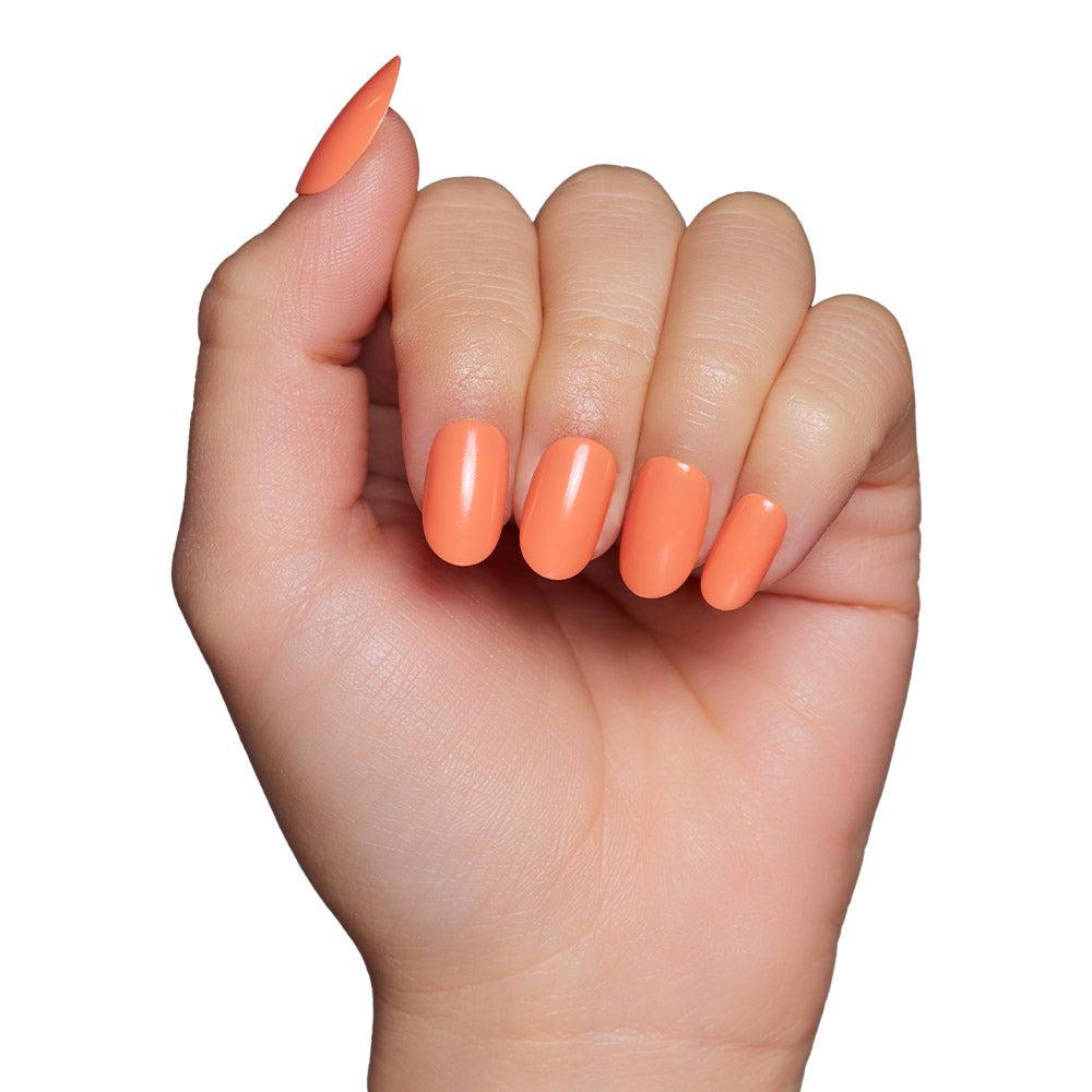 A hand with medium-length almond-shaped nails wears the glamnetic Apricot press-on set, shown in a glossy peach-orange polish against a white background. - Product image
