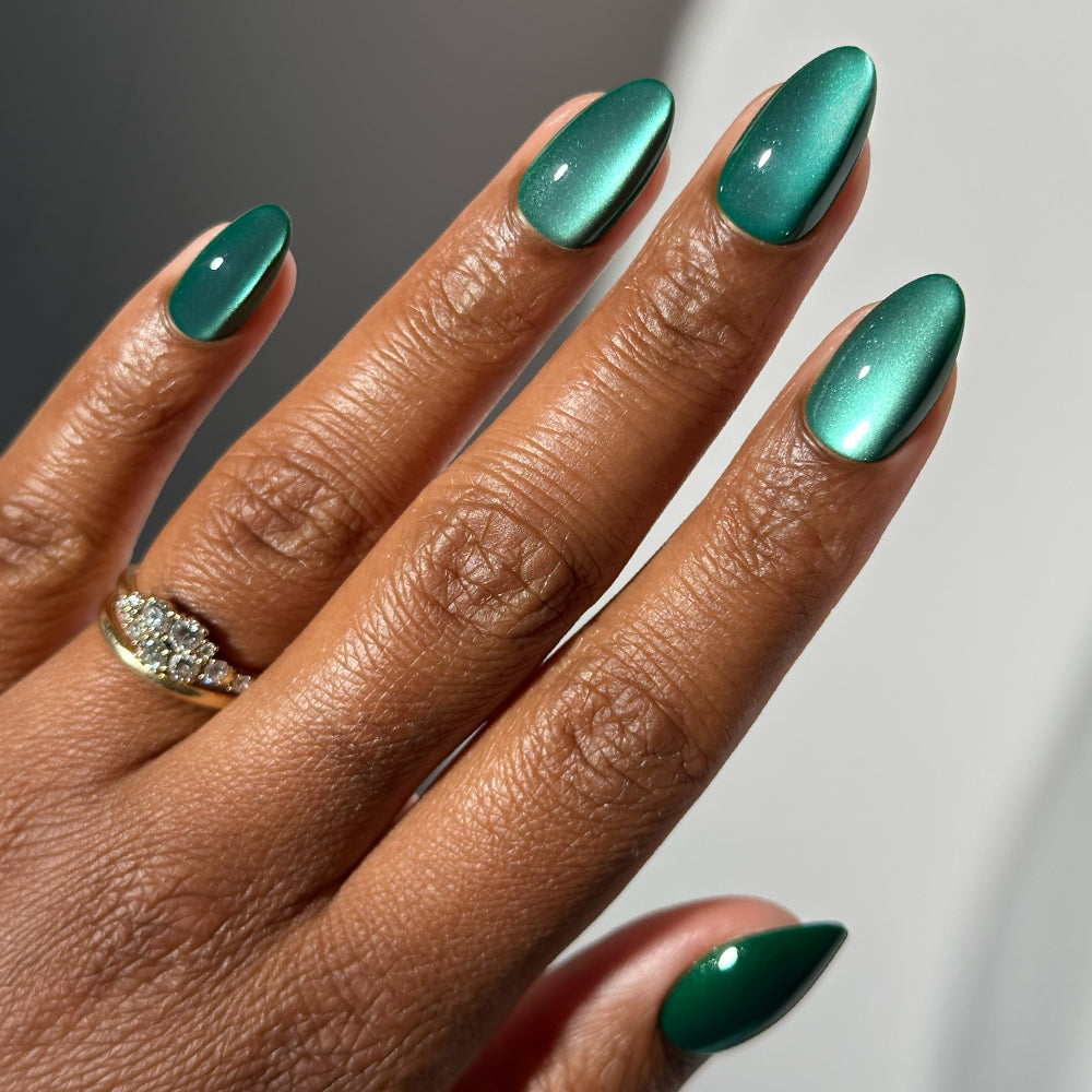 Hand with short almond nails painted in Arctic Aurora, a metallic, shimmery emerald green finish.