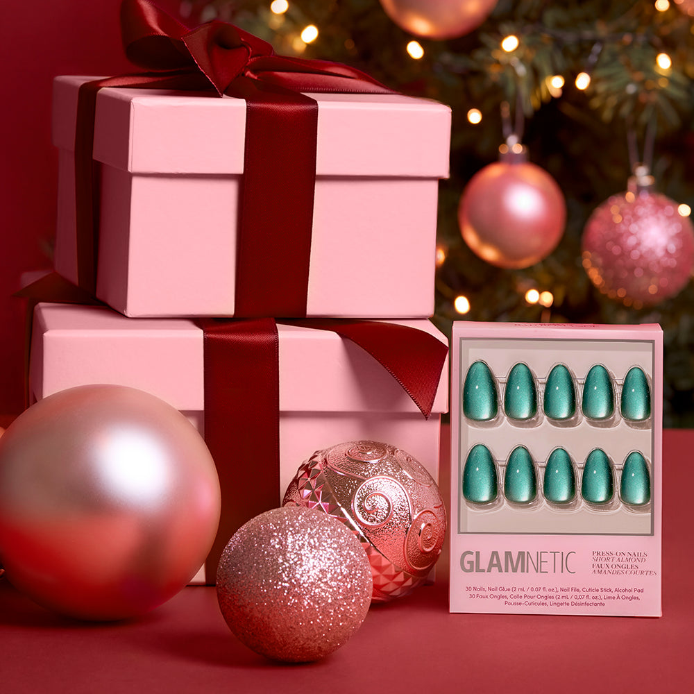 Arctic Aurora - A box of Glamnetic Arctic Aurora short almond emerald green press-on nails in a holographic teal finish, displayed next to wrapped gift boxes and decorative ornaments.