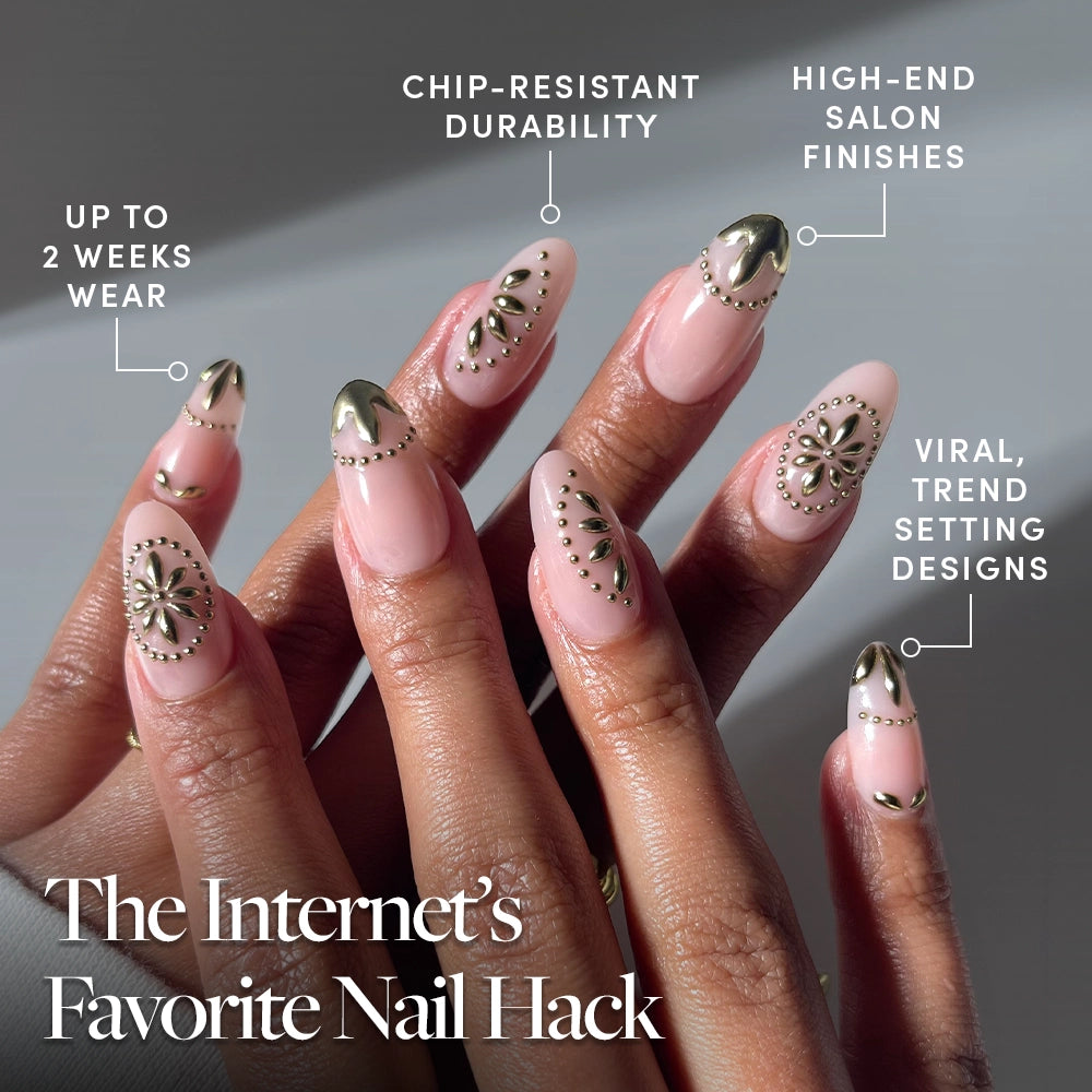 A close-up of hands with long, almond-shaped glamnetic Athenian Gold press-on nails featuring pink polish, metallic gold tips, and gold studs. Enjoy chip resistance, up to two-week wear, and salon-quality finishes. - Product image