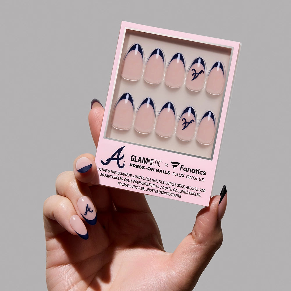 A hand with navy-tipped press-on nails holds a box of Glamnetic Atlanta Braves Press-On Nail Set, featuring a nude base, navy tips, and the iconic “A” logo for striking MLB-inspired nail art. - Product image