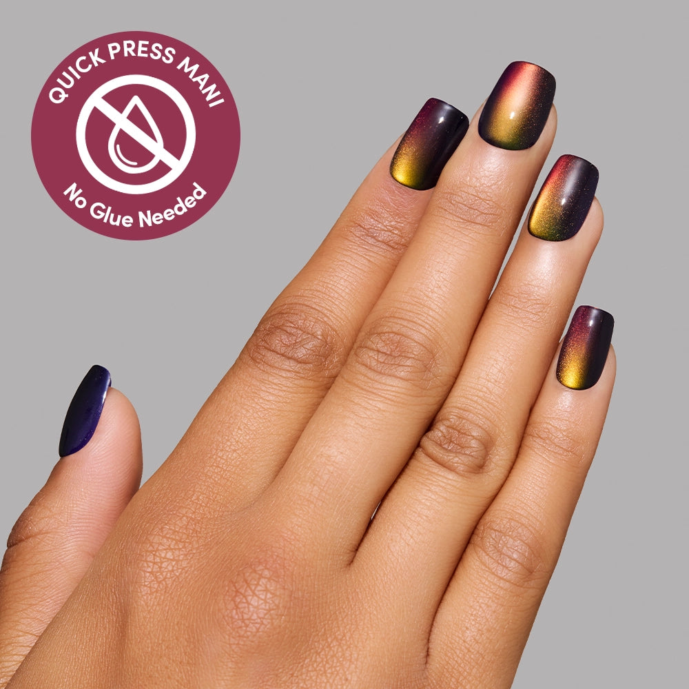 A hand adorned with glamnetic Aura Reading press-on nails in metallic ombré shades of yellow, orange, and purple displays an effortless manicure achieved in seconds—no glue needed, just stick them on for instant style. A circular label features the text: QUICK PRESS MANI, No Glue Needed. - Product image