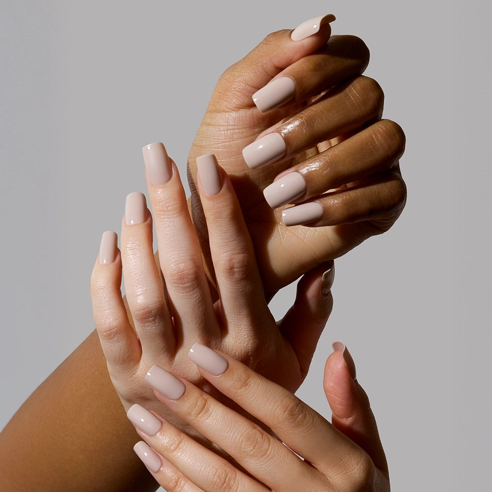 Three hands with varying skin tones showcase glamnetics Bare Bliss nude nail set, each featuring medium square, manicured nails. The subtle elegance of the polish stands out against a plain light gray backdrop. - Product image