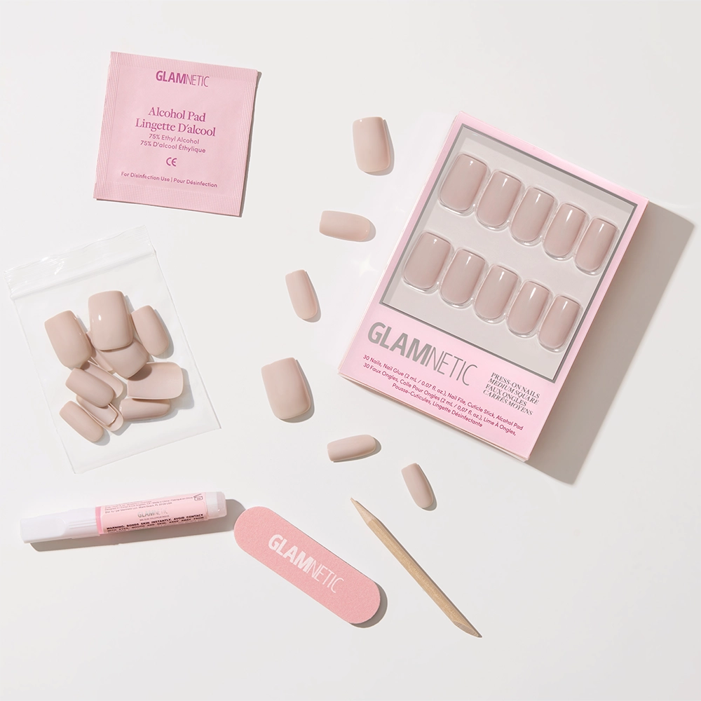 Bare Bliss by glamnetic features nude medium square press-on nails with an opaque finish, a pink nail file, cuticle stick, glue, alcohol pad, and extra nails—all neatly arranged on a white background. - Product image