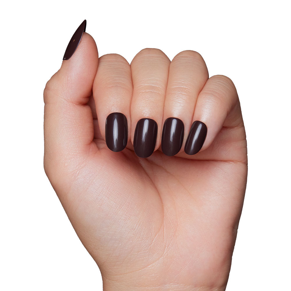 A hand with medium-length oval nails painted in glamnetics Bark Brown, a glossy dark brown polish, captures cozy vibes of a brown nail set against a white background. - Product image