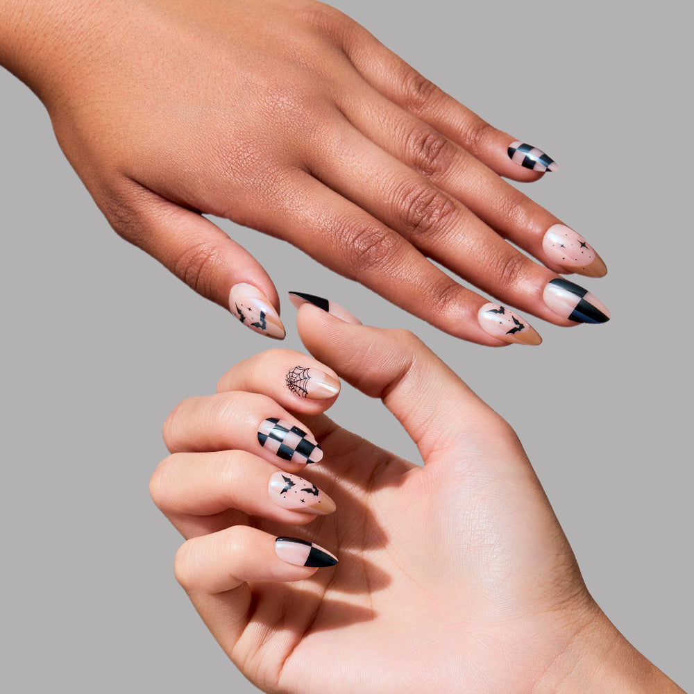 Two hands with manicured nails featuring black abstract designs—checkerboard, lines, and geometric tips—on a nude base show off a salon-quality mani created with glamnetic’s Bat Check Press-On Nail Set in a short almond shape, all set against a plain gray background. - Product image