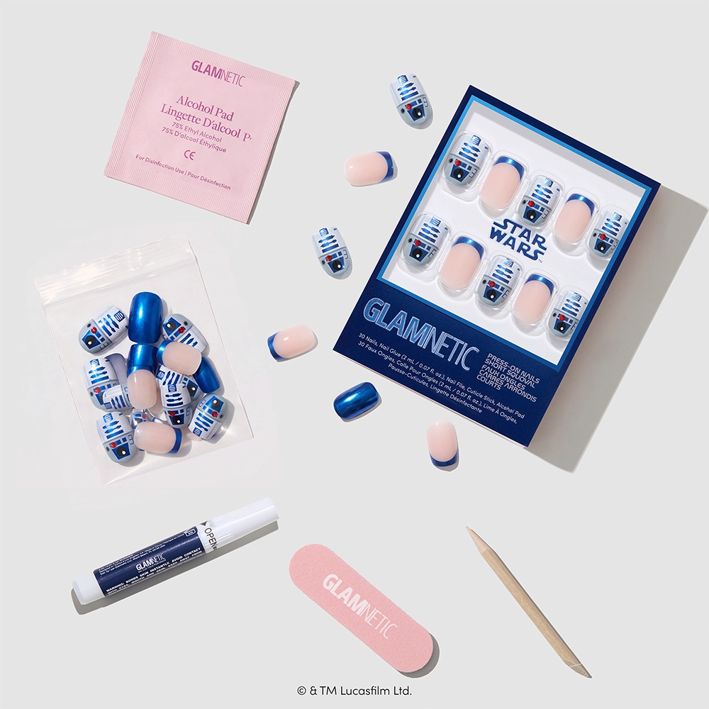 Beep-Boop by glamnetic: This STAR WARS-inspired press-on nail set features short squoval nails with an R2-D2 design, plus essential manicure tools including a nail file, cuticle stick, glue, alcohol pad, and a display box for the nails—all arranged on a light surface. Perfect for fans looking to add some Beep-Boop press-on nails from glamnetic to their collection. - Product image