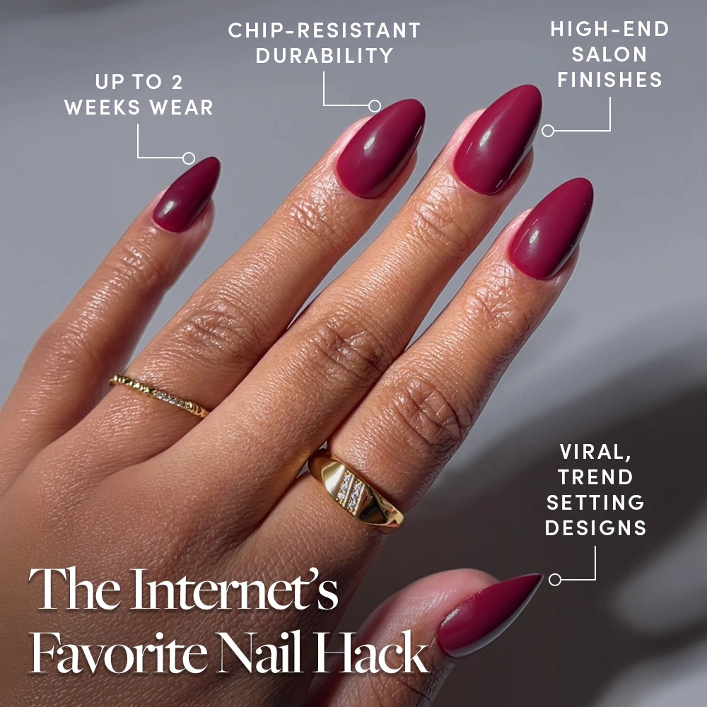 A hand with long, almond-shaped Berry Kiss maroon press-on nails by glamnetic wears gold rings. Text highlights up to 2 weeks wear, chip-resistant durability, high-end salon finish, and viral trend-setting designs. - Product image
