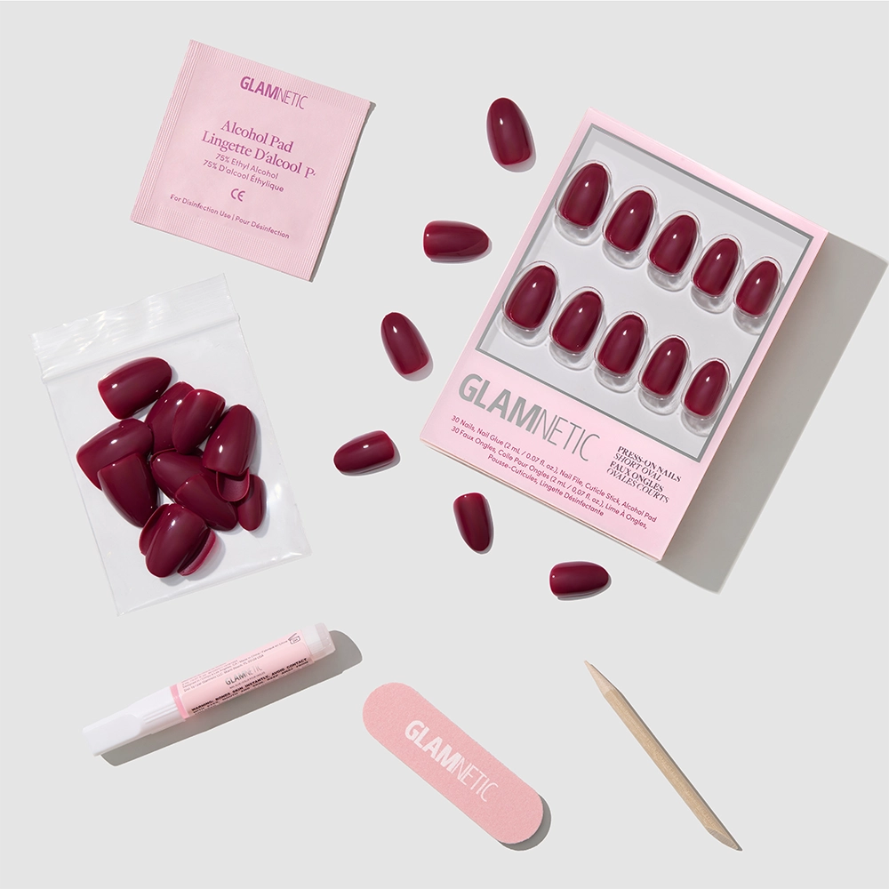 Berry Mood by glamnetic: glossy maroon press-on nails with nail glue, alcohol pad, nail file, and cuticle stick—all arranged on a light gray surface.