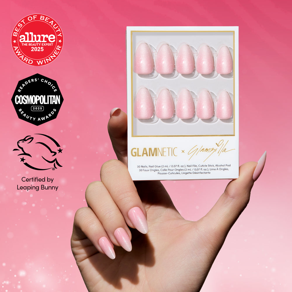 A hand with long, baby pink press-on nails holds a box of glamnetic BIG BUNNY ENERGY nails. Award logos for Allure, Cosmopolitan, and Leaping Bunny certification are shown on a sparkling pink glittery background.